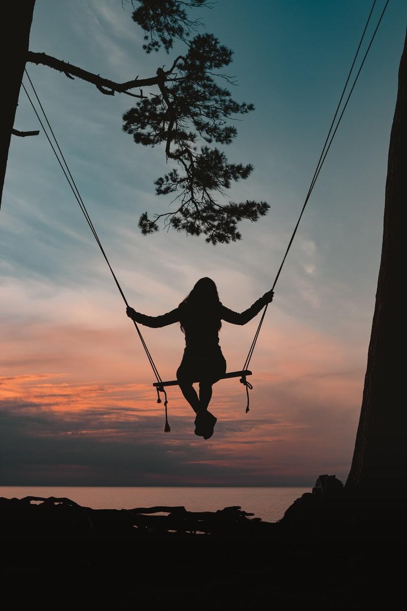 silhouette of person sitting on swing during sunset